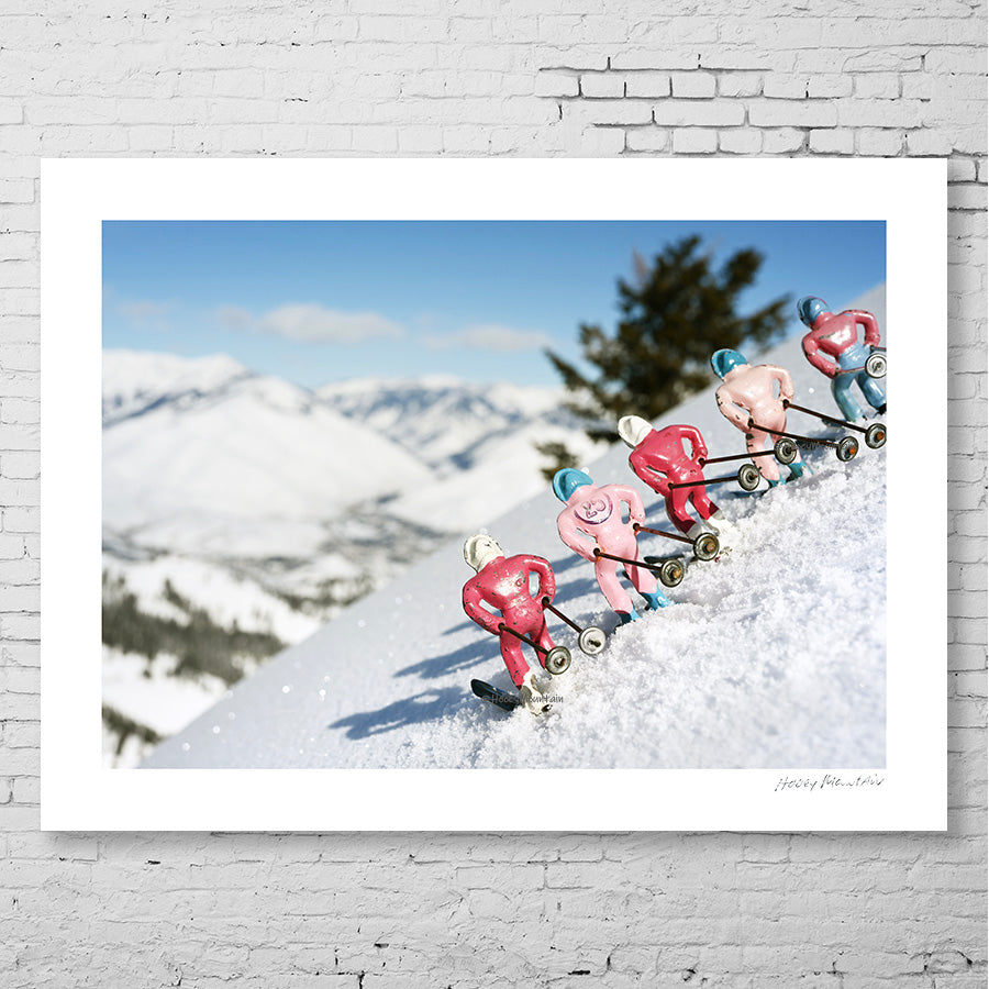 Pink toy skiers looking at the snowy mountain view. Photo by Hooey Mountain
