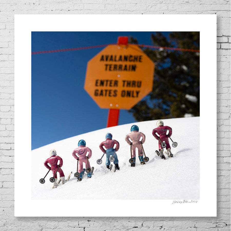 Five pink toy skiers by an avalanche sign by photographer Hooey Mountain