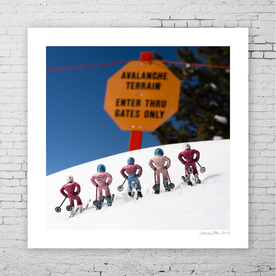 Five pink toy skiers by an avalanche sign by photographer Hooey Mountain